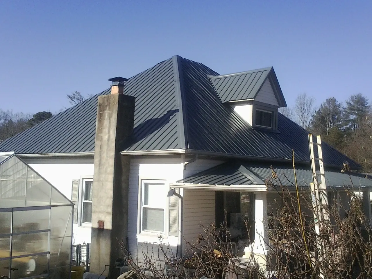 Dark blue standing seam metal roof on a white farmhouse with dormer — Slate & Tile Roof Repair by Roofing Brothers in Andreas