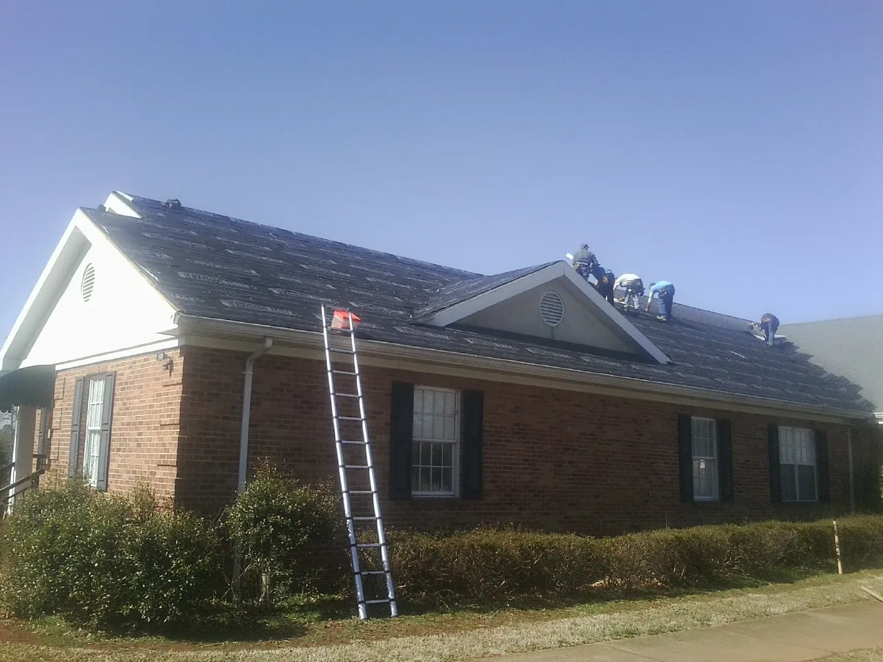 Crew tearing shingles off a brick ranch roof with a ladder set — Metal Roof Repair work by our crew in Andreas
