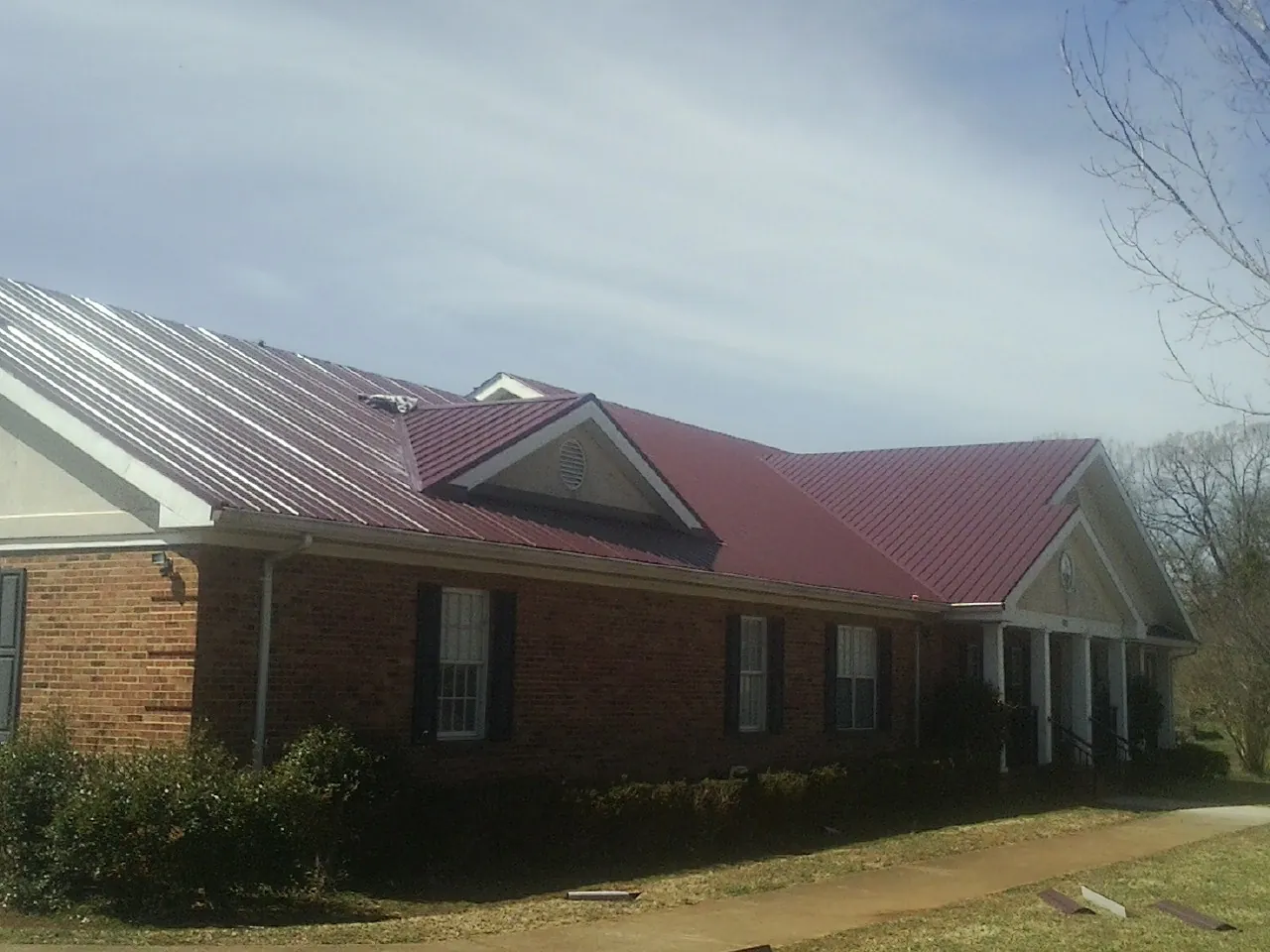 Red metal roof with gabled entries on a long brick building, from a Hail Damage Roof Repair job in Andreas