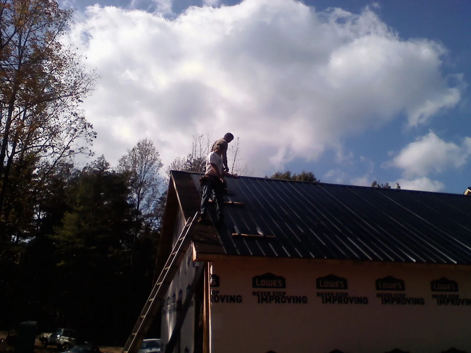 Roofer fastening dark metal panels high against a cloudy sky, from a Roof Inspection job in Andreas