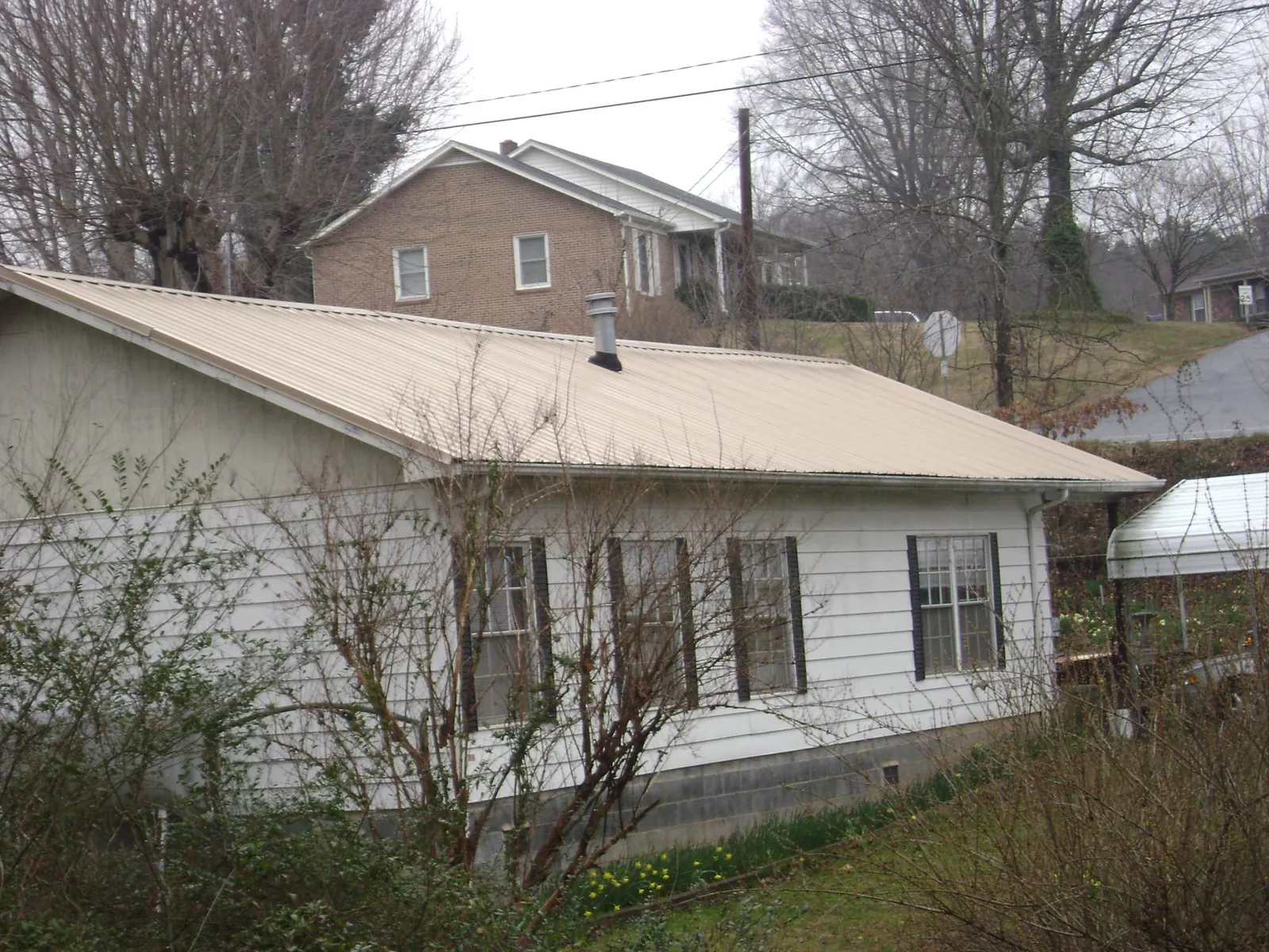 Tan metal roof on a white sided house set into a hillside — Commercial Roofing by Roofing Brothers in Andreas
